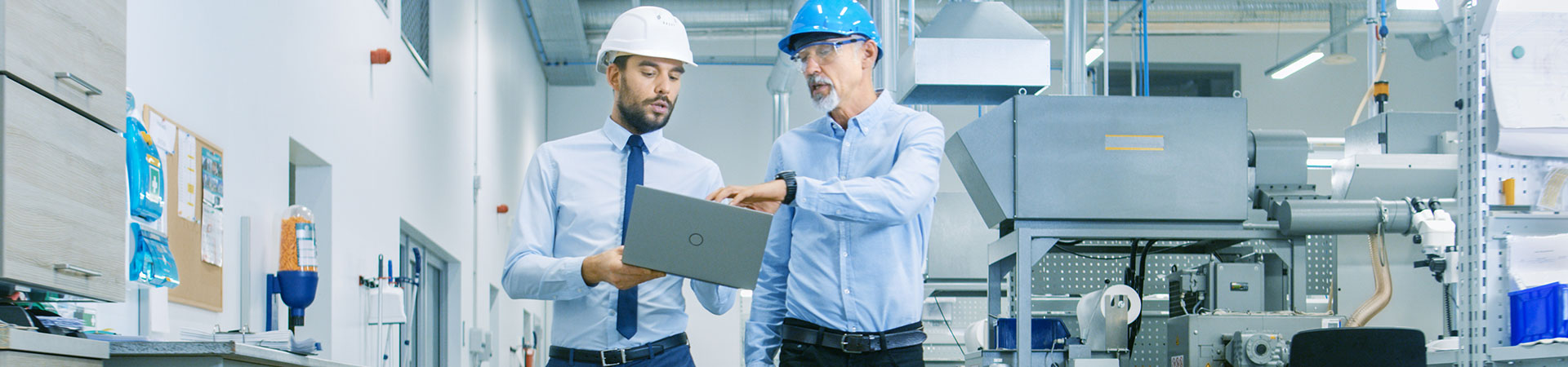 Zwei Männer in einer Werkshalle, die auf einen Laptop schauen
