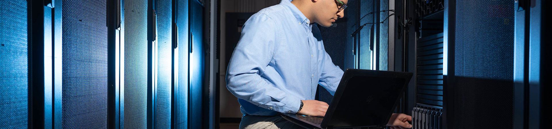 Mann mit Laptop im Serverraum, der zum Server hinschaut