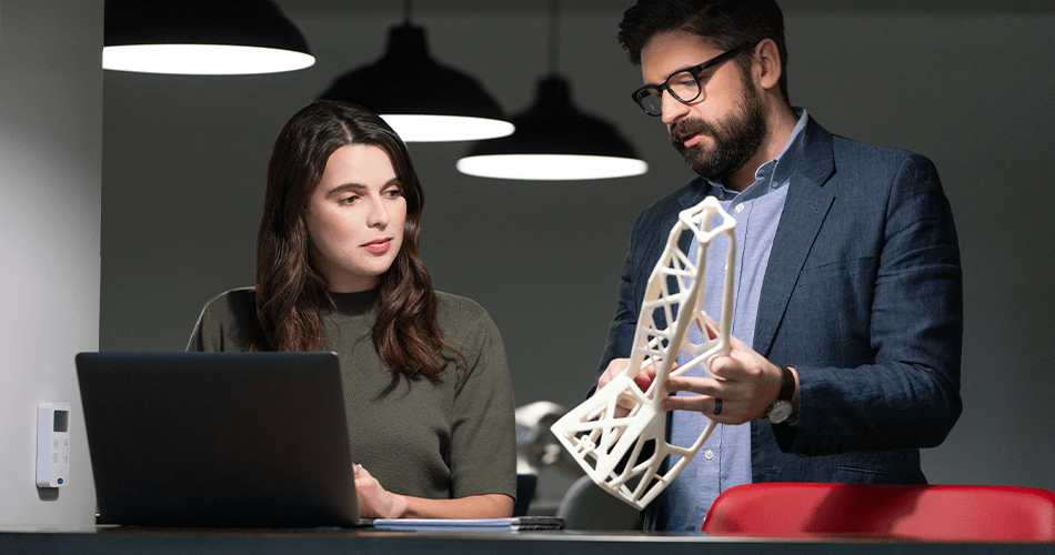 Mann, der einer Frau mit einem Laptop ein 3D-gedrucktes Teil zeigt